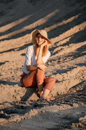 Young beautiful lonely woman with long hair in with straw hat. A lonely girl goes down the sand dunes. Summer fashion portrait outdoor.の写真素材