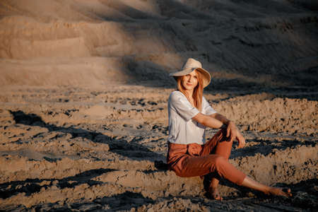 Young beautiful lonely woman with long hair in with straw hat. A lonely girl goes down the sand dunes. Summer fashion portrait outdoor.の写真素材