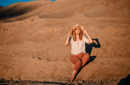 Young beautiful lonely woman with long hair in with straw hat. A lonely girl goes down the sand dunes. Summer fashion portrait outdoor.の写真素材