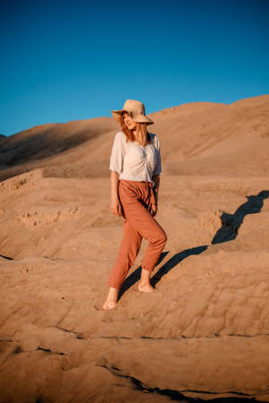 Young beautiful lonely woman with long hair in with straw hat. A lonely girl goes down the sand dunes. Summer fashion portrait outdoor.の写真素材