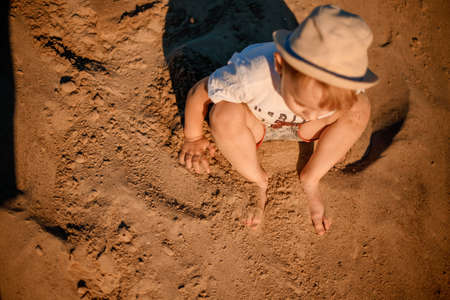 A little pretty boy in on a mountain of sand and plays. Focus legs. On a mountain of sand in the summer. Active son shows his skills.の写真素材