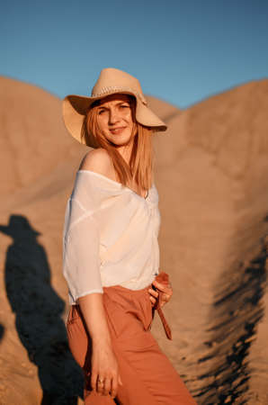 Young female exploring sandy beach with hat. Hipster girl, young traveler in nature desert. A woman walks in the desert to meet.の写真素材