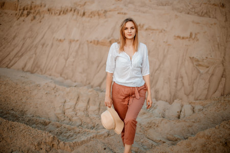 Young female exploring sandy beach with hat. Hipster girl, young traveler in nature desert. A woman walks in the desert to meet.の写真素材