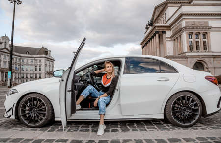 Young attractive model is sitting near the car. Girl sitting near a car. sensual girl enjoying sunset. Traveling.の写真素材
