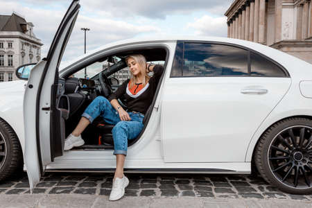 Young attractive model is sitting near the car. Girl sitting near a car. sensual girl enjoying sunset. Traveling.の写真素材