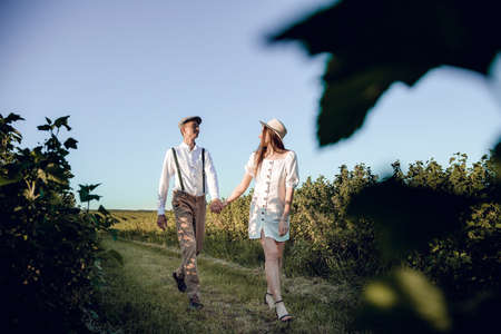 Young beautiful couple in love sitting and hugging in a green field with bushes. Walking in the green field on a sunny summer day.の写真素材