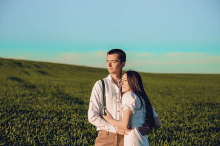 Young beautiful couple in love sitting and hugging in a green field with bushes. Walking in the green field on a sunny summer day.の写真素材