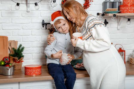Pregnant mother and her son enjoying in kitchen and christmast time. Pregnant woman with son on New Year's holidays.の写真素材