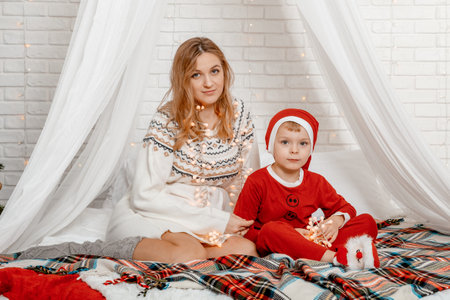 Happy Pregnant mother and son looking at camera in christmas lying on a couch on the bed. Pregnant mother and son in on the bed. New Year's decor. Cristmast Time.の写真素材