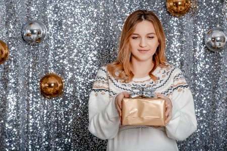 Baby Shower Concept. Happy Pregnant Lady Holding Wrapped Gift Box Looking At Camera Standing. Tummy of a pregnant woman with a Christmas toy in her hands.の写真素材