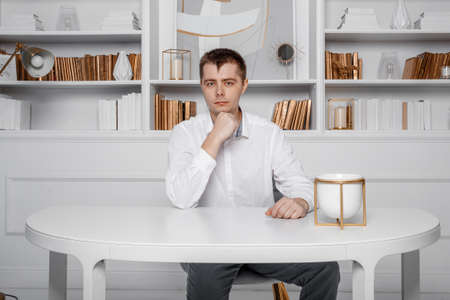 A man in a white shirt is sitting at a white table. Young business man on a desk. Attractive...