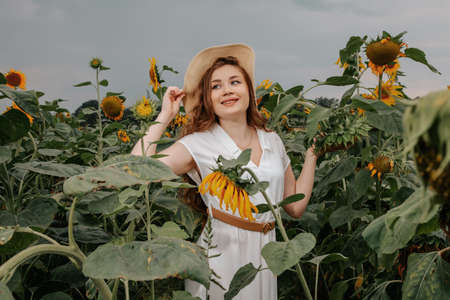 Beauty joyful teenage girl with sunflower enjoying nature and laughing on summer sunflower field. young girl in a field with sunflowers in a white dress with a hat.の写真素材