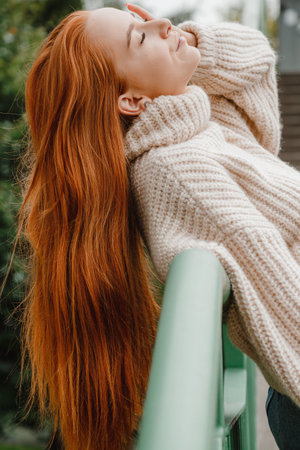 Red hair woman on street ladder. Red haired woman in stylish outfit. Fashion style girl with long...