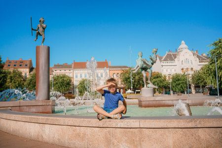 Child run and play on street fountain on Szombathely in Hungary. Boy have fun near fountain at...