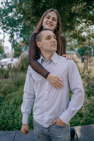 Happy couple in love enjoying a playful moment in the city park. A young man sitting on a bench...