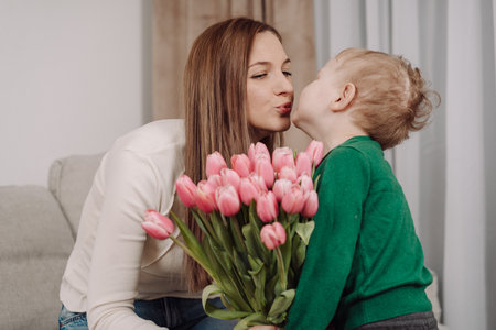 A smiling mother receives a bouquet of pink tulips from her young child. A touching moment of love and appreciation, perfect for celebrating International Women's Day and Mother's Day. Mother and son.の写真素材