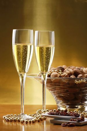 Glasses of champagne with gold background with walnuts, candels and dried raisinsの写真素材