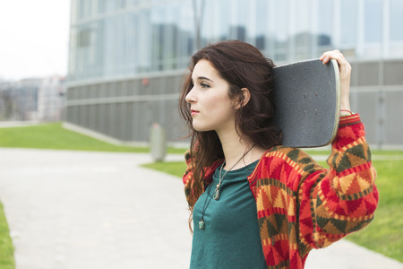 Closeup portrait of beautiful urban girl with skateboard in the street looking away.の写真素材