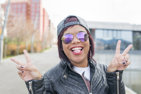Hipster excited beautiful latin woman with sunglasses showing her tongue in the street.の写真素材
