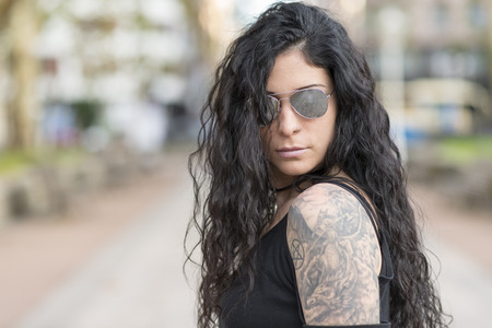 Urban portrait of beautiful tattooed woman with heavy metal style sunglasses.の写真素材