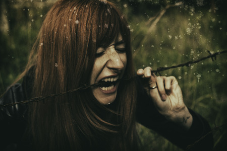 Girl with red hair sitting in front of barbed wire. Prison, jail, freedom concept.の写真素材