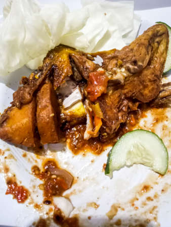 The chicken is a brownish yellow, placed on a white round plate, with two kinds of vegetables, namely cabbage, and cucumber, then added with hot chili sauce which is starting to run out.の写真素材