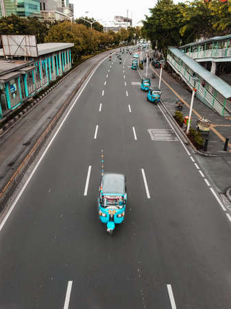 A domicile that crosses the highway, in front of itself, and is followed by many motorized vehicles behind it. Baja is a three-wheeled vehicle that is still widely used by people in the Indonesian.の写真素材
