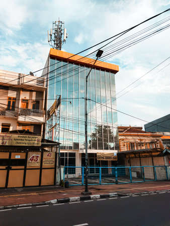 A building whose glass reflects the beautiful sky, the building is crushed by other buildings.の写真素材
