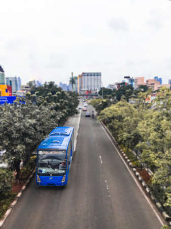 A bus trans Jakarta crosses the middle of Jakarta Indonesia's road, on the left and right of the road, there are shady trees, making the road more comfortable for vehicles to pass.のeditorial素材