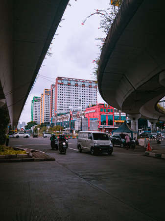 Jakarta Pusat, Indonesia - 14 February 2021: Many vehicles pass on the highway, which is located under two concrete bridges with a backdrop of colorful buildings.のeditorial素材