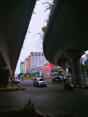 Jakarta Pusat, Indonesia - 14 February 2021: Many vehicles pass on the highway, which is located under two concrete bridges with a backdrop of colorful buildings.のeditorial素材