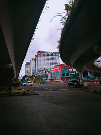 Jakarta Pusat, Indonesia - 14 February 2021: Many vehicles pass on the highway, which is located under two concrete bridges with a backdrop of colorful buildings.のeditorial素材