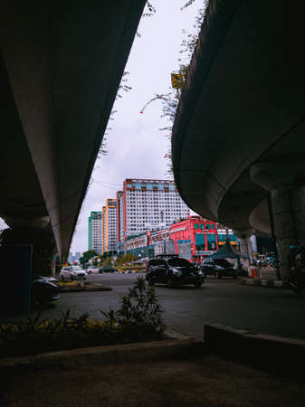 Jakarta Pusat, Indonesia - 14 February 2021: Many vehicles pass on the highway, which is located under two concrete bridges with a backdrop of colorful buildings.のeditorial素材
