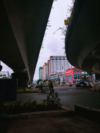 Jakarta Pusat, Indonesia - 14 February 2021: A drink seller is crossing the highway under two concrete bridges against a backdrop of colorful buildingsのeditorial素材