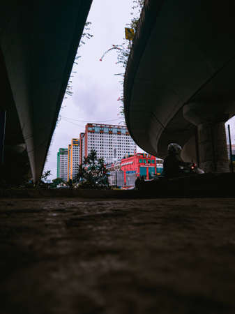 Jakarta Pusat, Indonesia - 14 February 2021: Many vehicles pass on the highway, which is located under two concrete bridges with a backdrop of colorful buildings.のeditorial素材