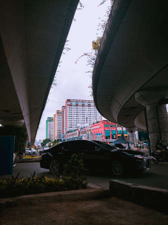 Jakarta Pusat, Indonesia - 14 February 2021: Many vehicles pass on the highway, which is located under two concrete bridges with a backdrop of colorful buildings.のeditorial素材