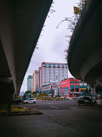 Jakarta Pusat, Indonesia - 14 February 2021: Many vehicles pass on the highway, which is located under two concrete bridges with a backdrop of colorful buildings.のeditorial素材