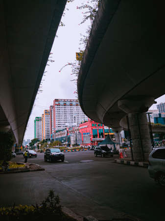 Jakarta Pusat, Indonesia - 14 February 2021: Many vehicles pass on the highway, which is located under two concrete bridges with a backdrop of colorful buildings.のeditorial素材