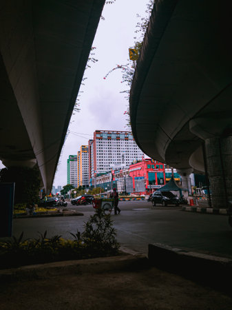 Jakarta Pusat, Indonesia - 14 February 2021: A drink seller is crossing the highway under two concrete bridges against a backdrop of colorful buildingsのeditorial素材
