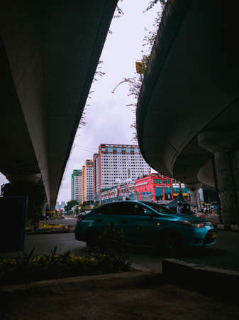 Jakarta Pusat, Indonesia - 14 February 2021: Many vehicles pass on the highway, which is located under two concrete bridges with a backdrop of colorful buildings.のeditorial素材