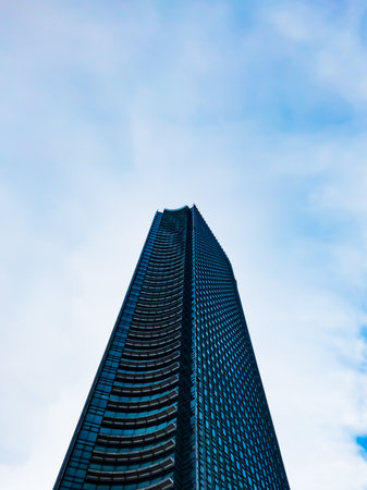 Central Jakarta, Indonesia - March 21th, 2021: A tall blue building under a clear sky with fluffy clouds.のeditorial素材