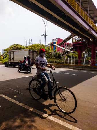 Central Jakarta, Indonesia - April 5th, 2021: An old man rides a bicycle on the highway during the day.のeditorial素材