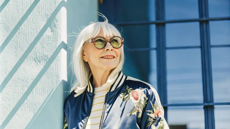 Stylish senior woman in sunglasses smiling outdoors.の素材