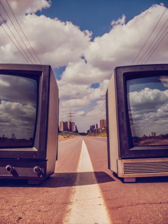 Vintage televisions on an empty road reflecting urban skyline.の素材