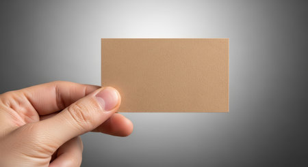 Hand holding blank card against gradient gray background for branding or mockupの素材