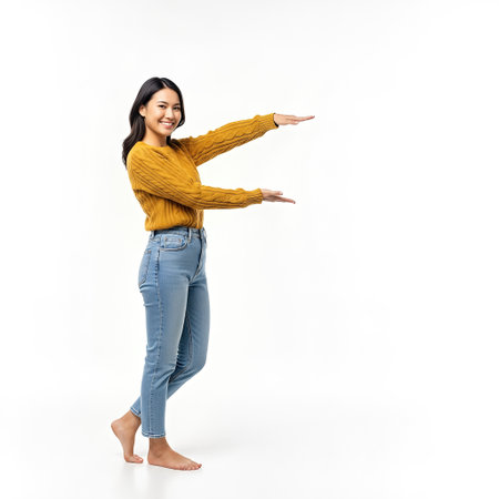 Cheerful young woman in yellow sweater gesturing enthusiastically on white background.の素材