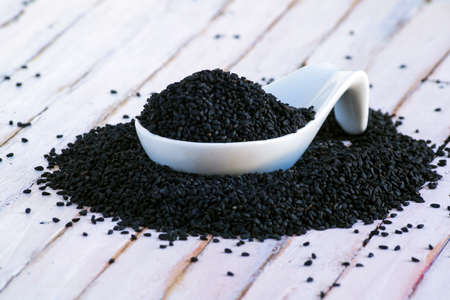 Porcelain Spoon full of black seeds on rustic wooden Background. Macro shot.の写真素材