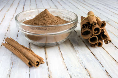 Cinnamon sticks and glass bowl full of Cinnamon powder on rustic wooden background.の写真素材