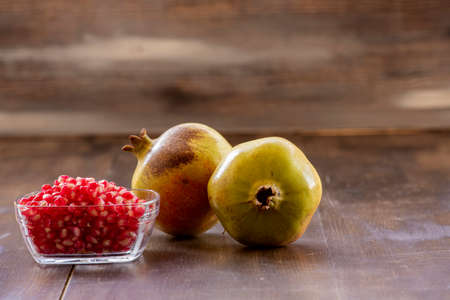 Pomegranate seeds in bowl and pomegranate on wooden background