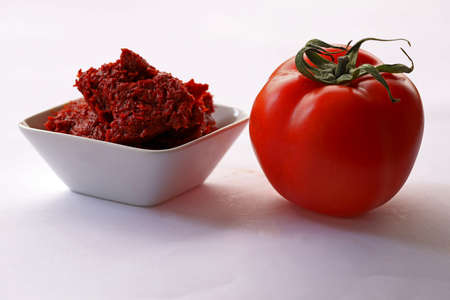 Tomatoes on white background and tomato paste in bowl.